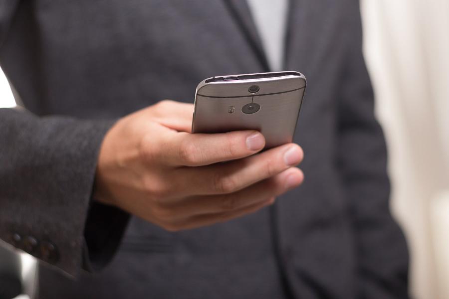 Man sieht den Oberörber eines Mannes, der ein Smartphon ein der einen Hand hält.