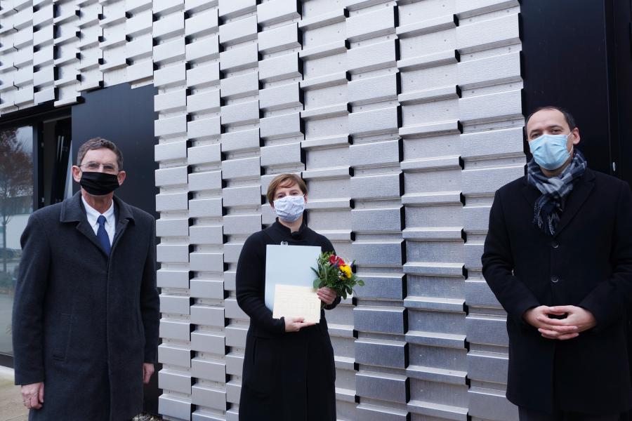 Zwei Herrn und eine Dame schauen in die Kamera. Im Hintergrund eine Fassade aus Metall.