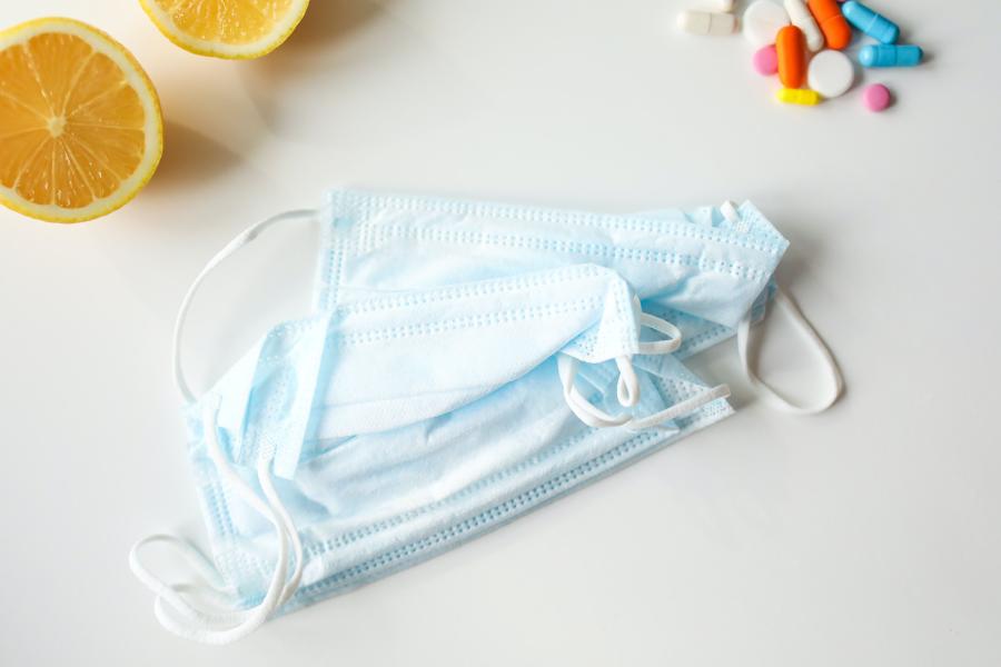 Hellblaue OP-Masken, Zitronenscheiben und einige Tabletten liegen auf einer hellen Fläche