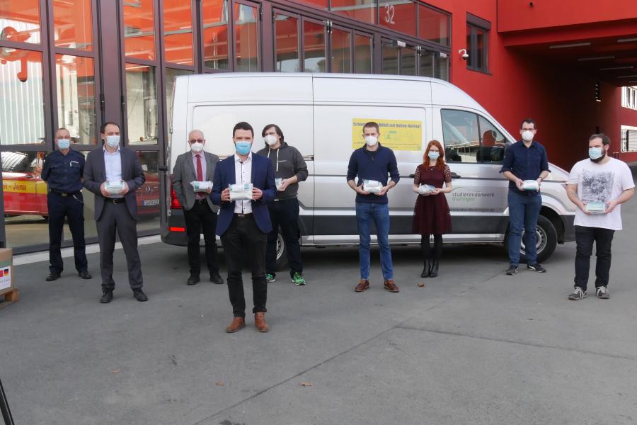 Viele Menschen vor einem Fahrzeug, alle tragen eine Maske