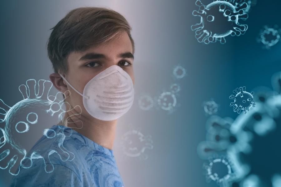 Ein junger Mann trägt eine medizinische Maske, davor symbolische Coronaviren