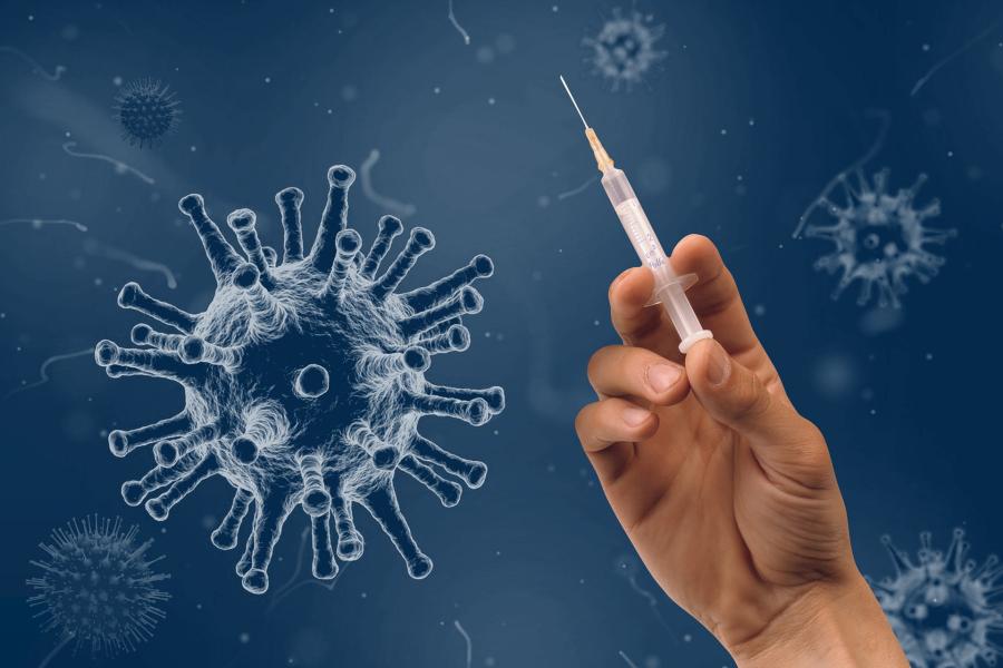 Hand hält eine Spritze, daneben das Coronavirus als blaue Kugel mit vielen Ausstülpungen in Großaufnahme