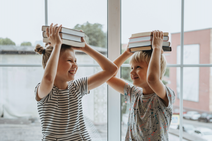 Zwei Kinder haben Bücher auf den Kopf und machen Faxen 