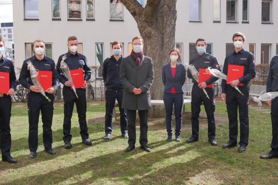 Acht Männer und eine Frau schauen in die Kamera, alle tragen Masken