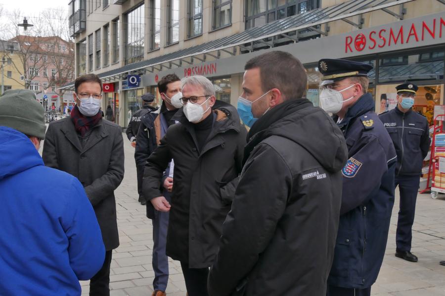 Fünf Menschen stehen in einer Straße mit vielen Läden, um Sie einige Polizisten und Journalisten