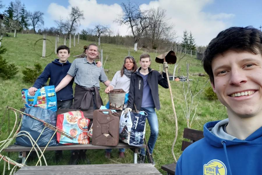 Fünf Menschen stehen auf einer Wiese und halten Müllgegenstände in die Kamera