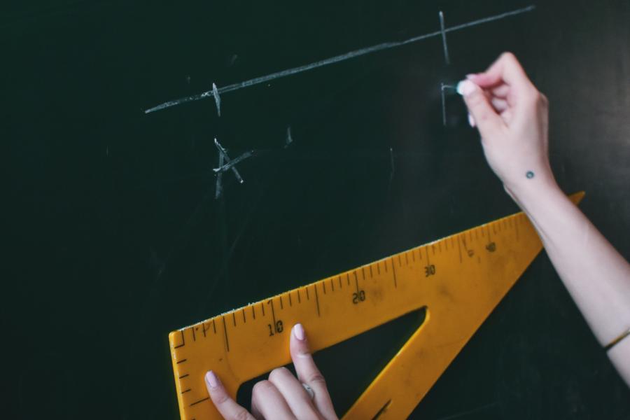 Zwei Hände halten ein Dreieck und schreiben eine geometrische Formel an die Tafel 