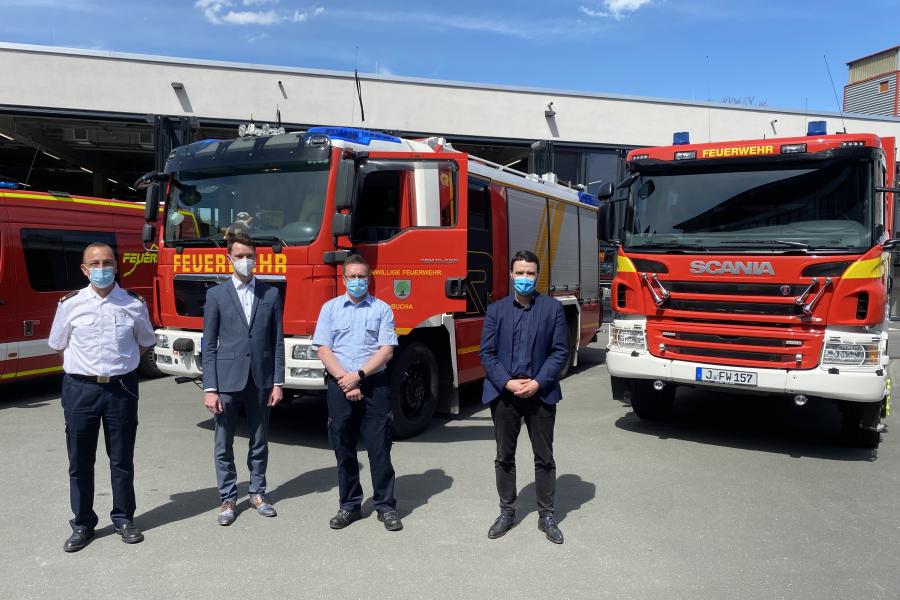 Feuerwehr im Hintergrund, im Vordergrund vier Männer mit Masken