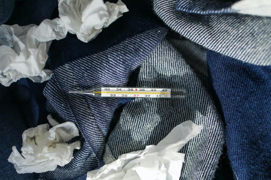 Ein Fieberthermometer und benutzte Taschentücher liegen auf Jeansstoff