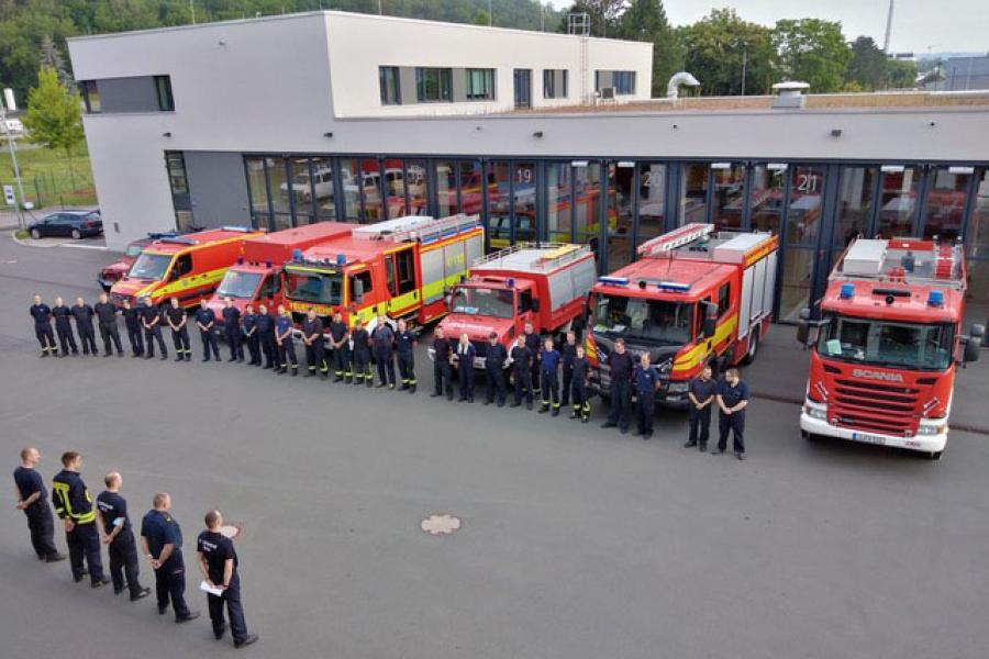 Etwa 30 Personen in Feuerwehrkleidung stehen vor 7 Feuerwehr-Fahrzeugen vor der Feuerwache Jena