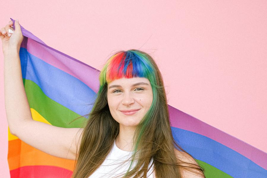 Eine Frau mit gefärbten Haaren hält eine Regenbogenfahne
