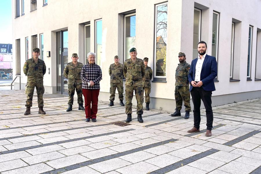 Mehrere Personen stehen im Außenbereich vor einem Gebäude. Einige tragen zivile Kleidung, einige tragen Bundeswehr-Uniform.