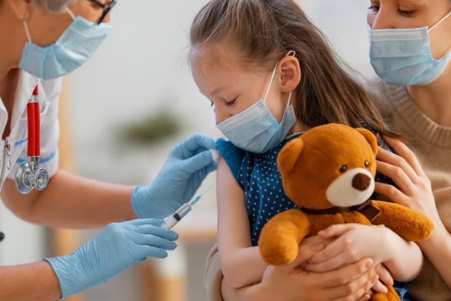 Ein Kind mit Teddy lässt sich impfen