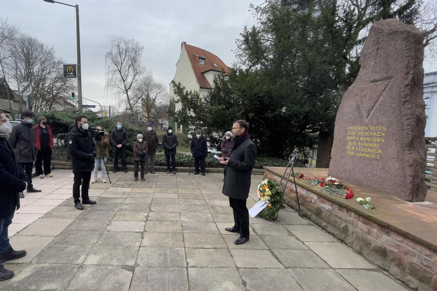 Menschen stehen vor einem Gedenkstein, ein Redner im Vordergrund