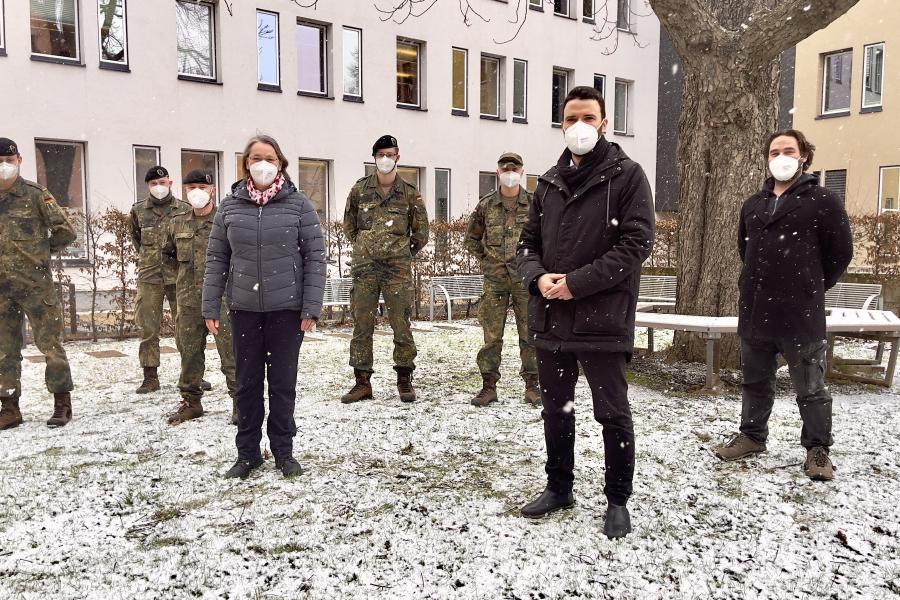 Menschen stehen in einer Schneelandschaft, darunter fünf Soldaten