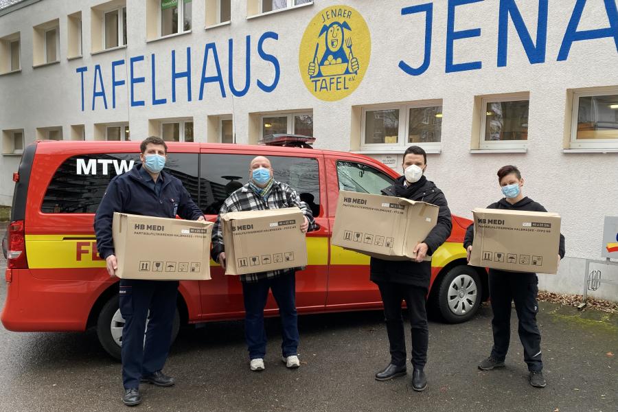 Vier Menschen mit Kisten vor einem Transporter der Feuerwehr