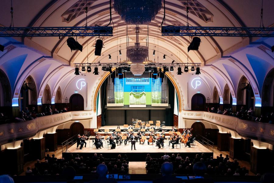 Blick in das Volksbad die Wände sind blau angeleuchtet in der Mitte die Bühne mit den Musiker:innen der Jenaer Philharmonie