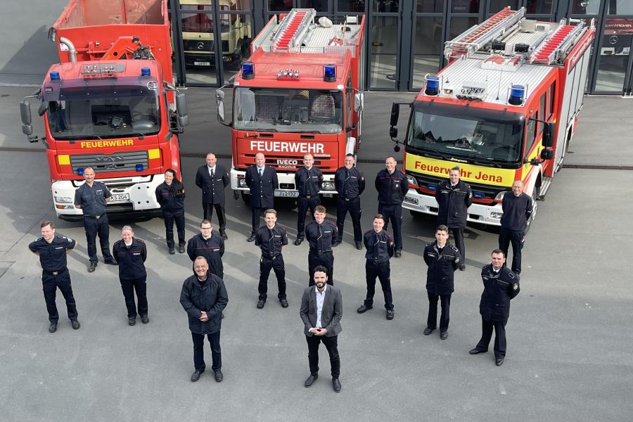 Feuerwehrleute in Uniform vor drei Feuerwehrfahrzeugen