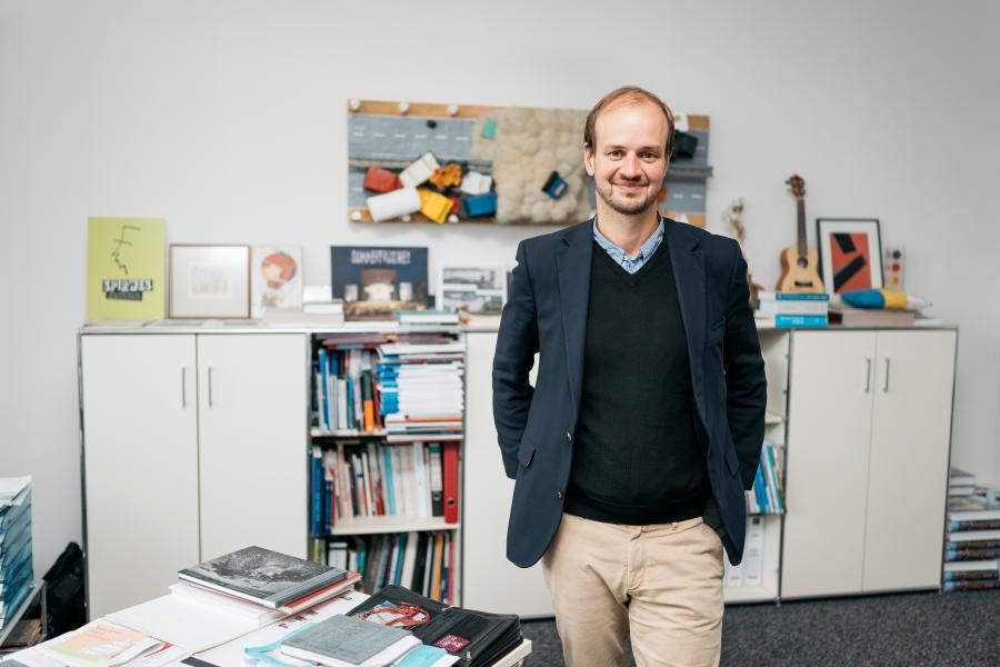 Jonas Zipf steht in seinem Büro vor einem Sideboard mit Büchern.