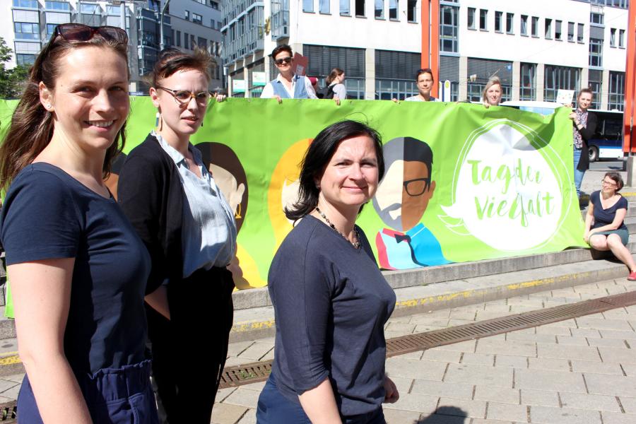 Drei Frauen stehen vor einem Plakat auf dem "Tag der Vielfalt" steht.