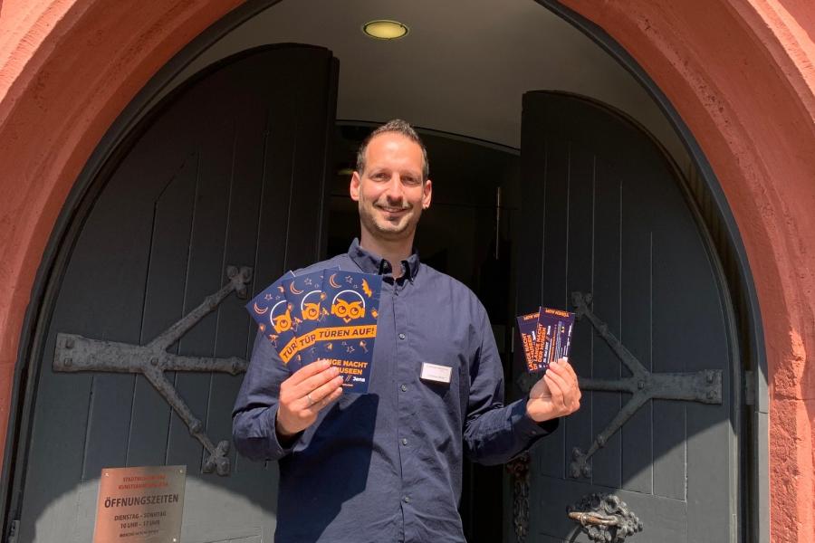 Christian Möller von den Städtischen Museen Jena steht vor einem Tor und hät Tickets in die Kamera.