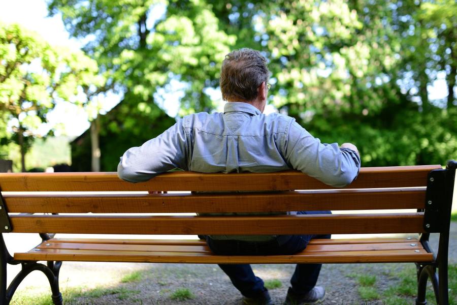 Ein älterer Mann sitzt auf einer Parkbank. Man sieht ihn von hinten.