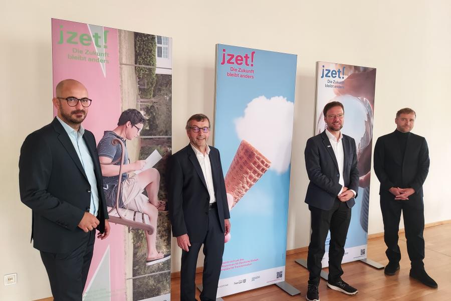 Vier Männer lächeln in die Kamera, im Hintergrund stehen Rollups.