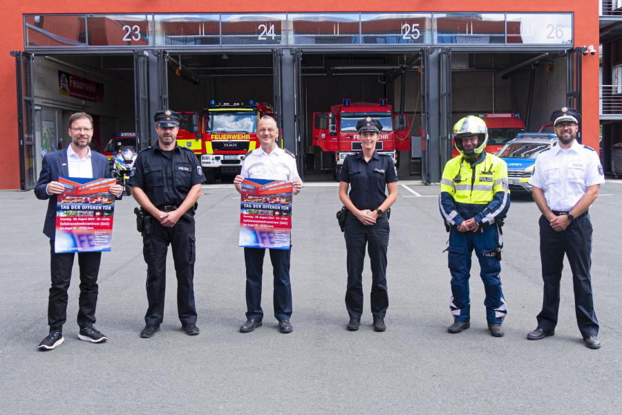 Feuerwehrleute und Polizisten vor einer Feuerwehr mit geöffneten Toren