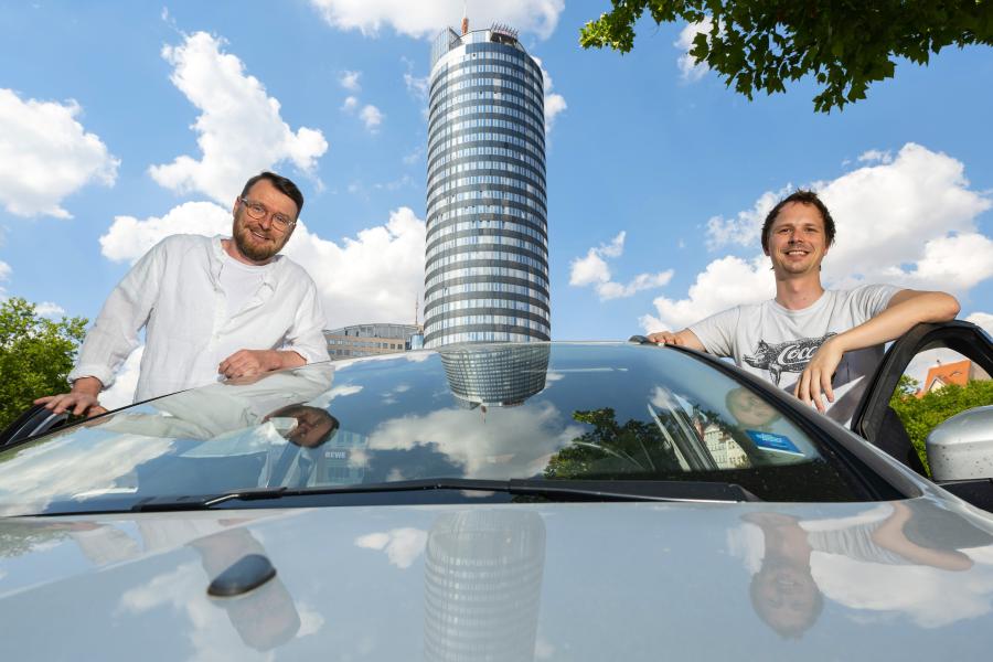 Zwei Männer und ein Auto, im Hintergrund der Jentower