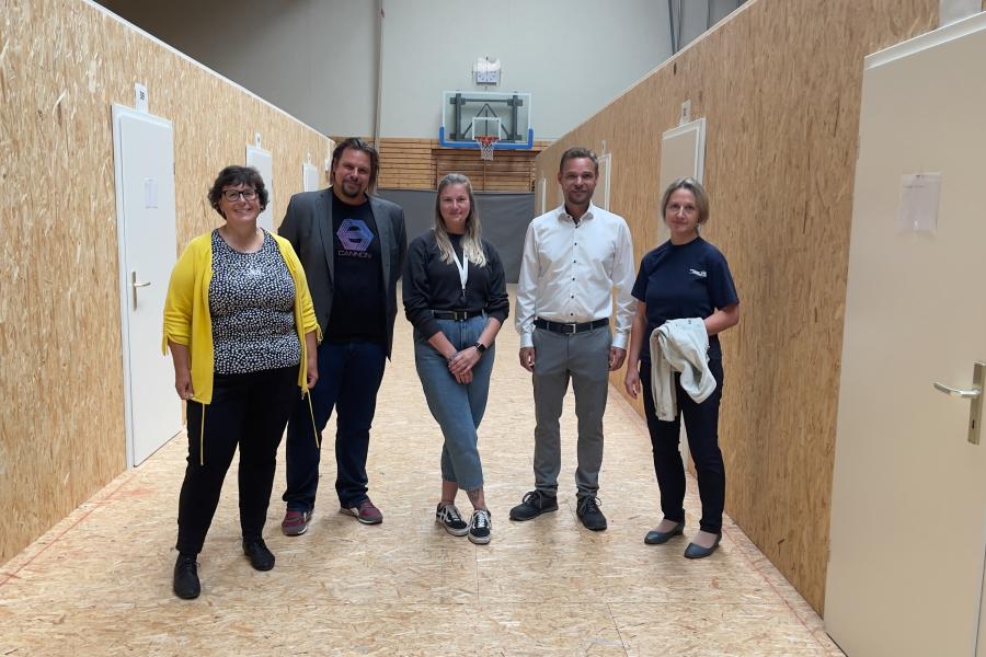 5 Personen in einer umgebauten Turnhalle schauen die Kamera