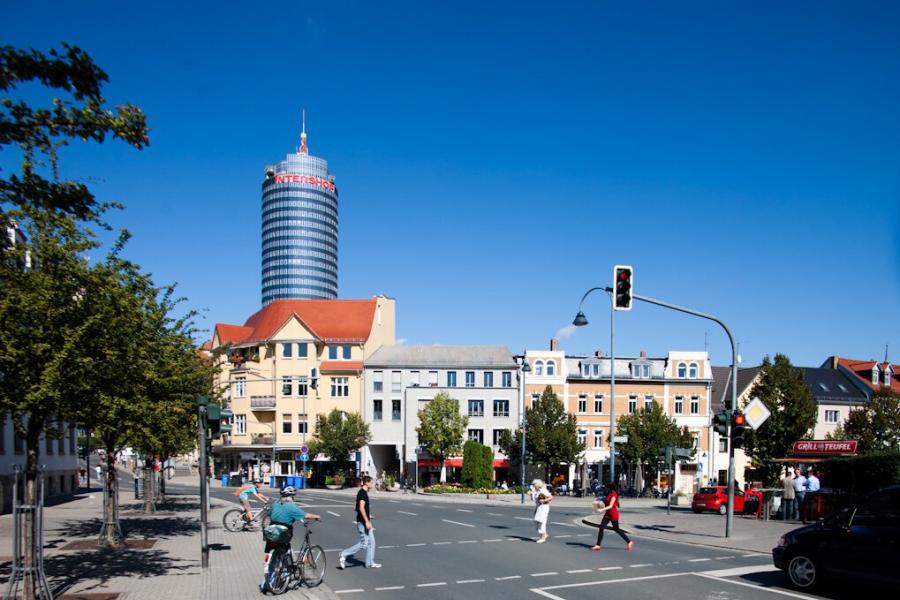 Menschen überqueren eine Straße an einer Ampelkreuzung, im Hintergrund ein großer Turm.