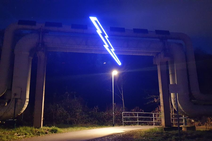 An einem Fernwärmerohr hängt eine LIcht-Installation in Form eines Blitzes.