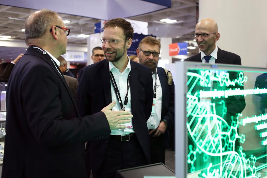 Vier Männer stehen an einem Stand auf einer Messe und unterhalten sich.