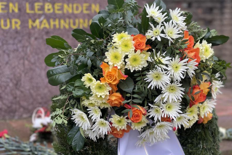 Ein Kranz mit Blumen vor einem Denkmal im Hintergrund
