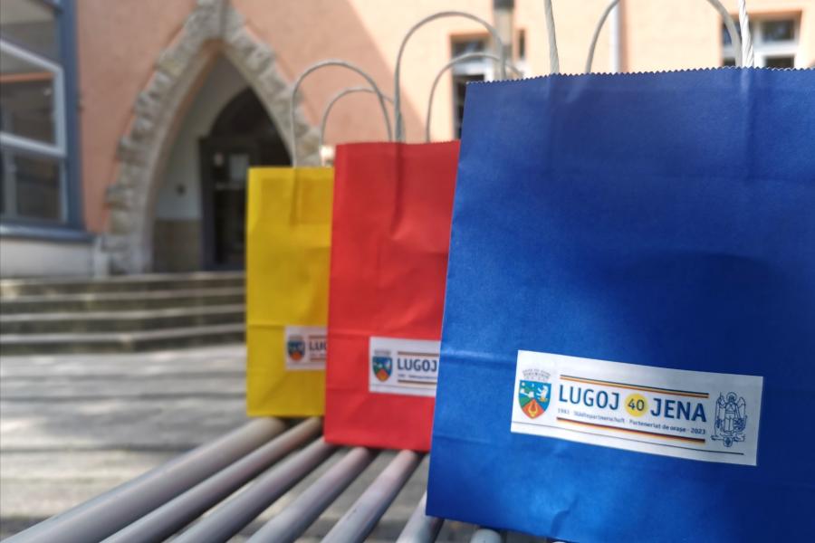 Drei Geschenketüten für die Gäste aus Lugoj stehen vor dem Gebäude Anger 15 auf einer Bank.: