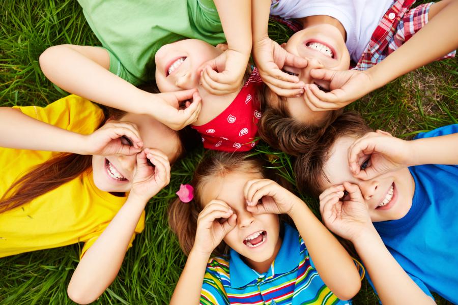 Fünf Kinder liegen im Kreis auf einer Wiese.