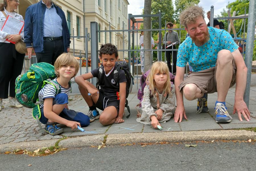 Die 7-jährigen Kinder Justus, Josef und Marla mit Erzieher Tino Buschbeck (v.l.) markieren ihren Schulweg mit Kreide. (Credit: Stadt Jena)