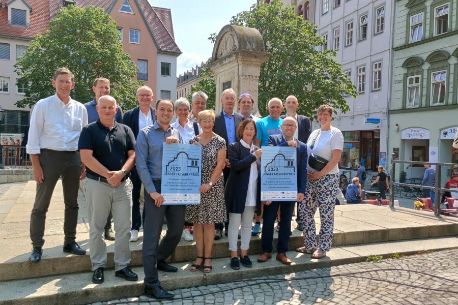 Bürgermeister Christian Gerlitz mit Sponsor*innen des Fassadenpreises stehen auf dem Jenaer Marktplatz am Brunnen.