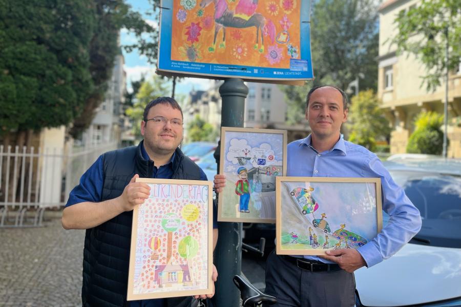 Zwei Männer zeigen Kunstwerke von Kindern
