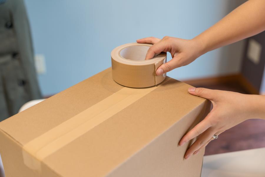 Eine Person schließt eine Box mit Paketband