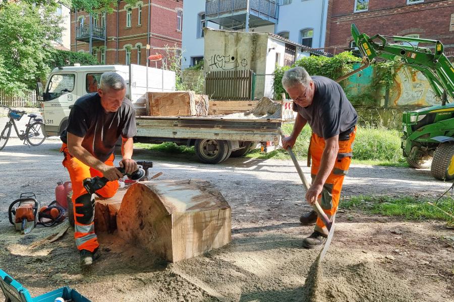 Zwei Männer stellen  große Scheiben eines Baumstammes zum Klettern auf.