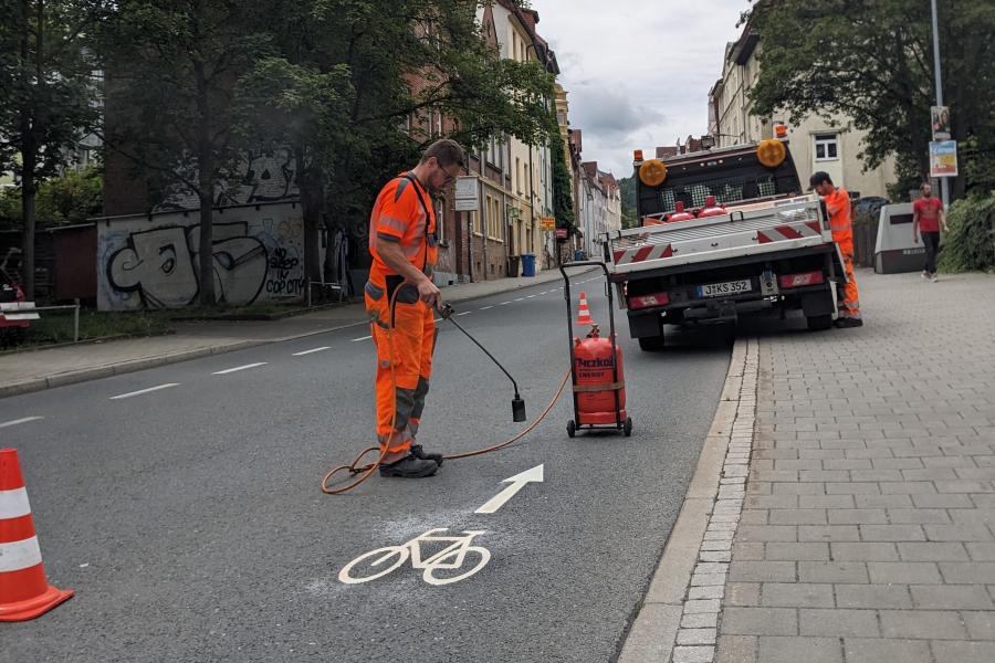 Ein Mitarbeiter vom Kommunalservice Jena bringt auf dem Magdelstieg ein Fahrrad-Piktogramm auf die Straße auf
