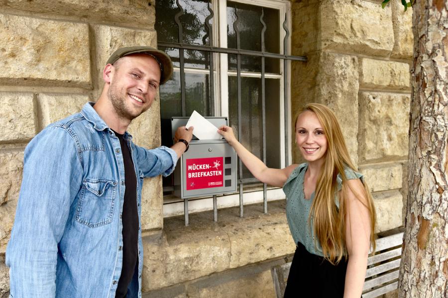 Zwei Personen stecken einen Briefumschlag in einen Kasten