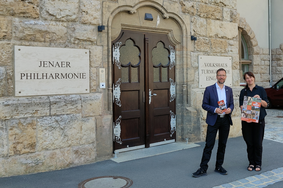 Oberbürgermeister Thomas Nitzsche und Elke Zimmermann, Teamleiterin Denkmalschutz der Stadt Jena, stehen vor dem Eingang des Volkshauses Jena  und halten einen Flyer bzw. ein Plakat des Denkmaltages 2024.