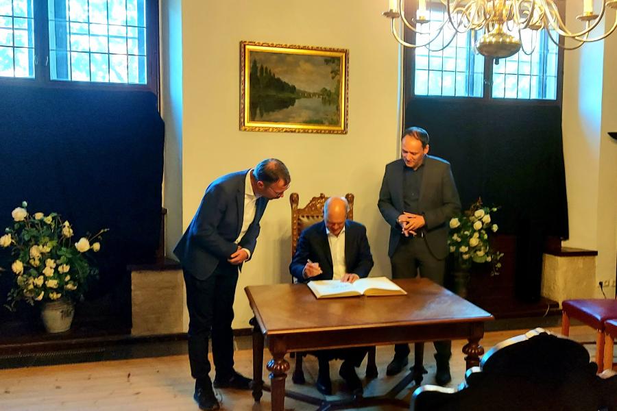 Olaf Scholz trägt sich ins Goldene Buch der Stadt Jena ein. Er sitzt am Tisch. Oberbürgermeister Dr. Thomas Nitzsche und Bürgermeister Christian Gerlitz stehen neben ihm.