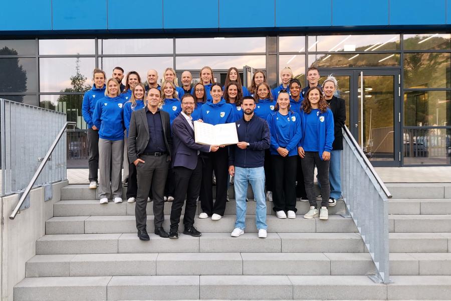 Menschen stehen auf einer Treppe, im Hintergrund ist das Stadion, zwei Personen halten das Goldene Buch der Stadt Jena aufgeklappt