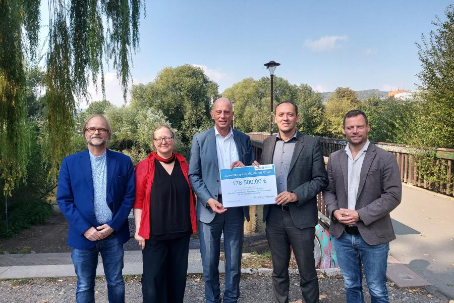 Fünf Personen stehen an der Griesbrücke in Jena. Ein Scheck wird von zwei Personen in der Hand gehalten