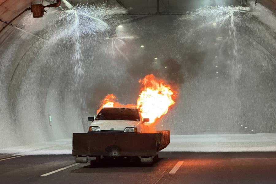 Ein Auto steht im Tunnel und brennt. Die Brandbekämpungsanlage versprüht Löschschaum.