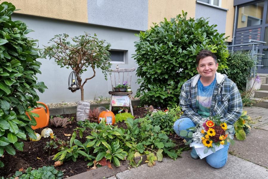 Preisträgerin Kathy Witte hockt neben einem Blumenbeet, welches zu der Grünen Oase gehört, die sie geschaffen hat.