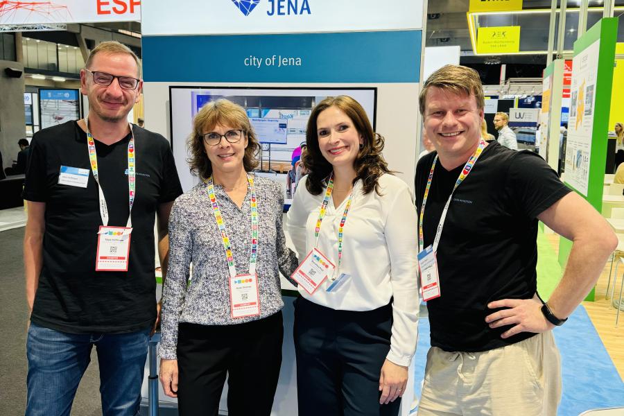 Vier Personen stehen vor einem Messestand und lächeln in die Kamera.
